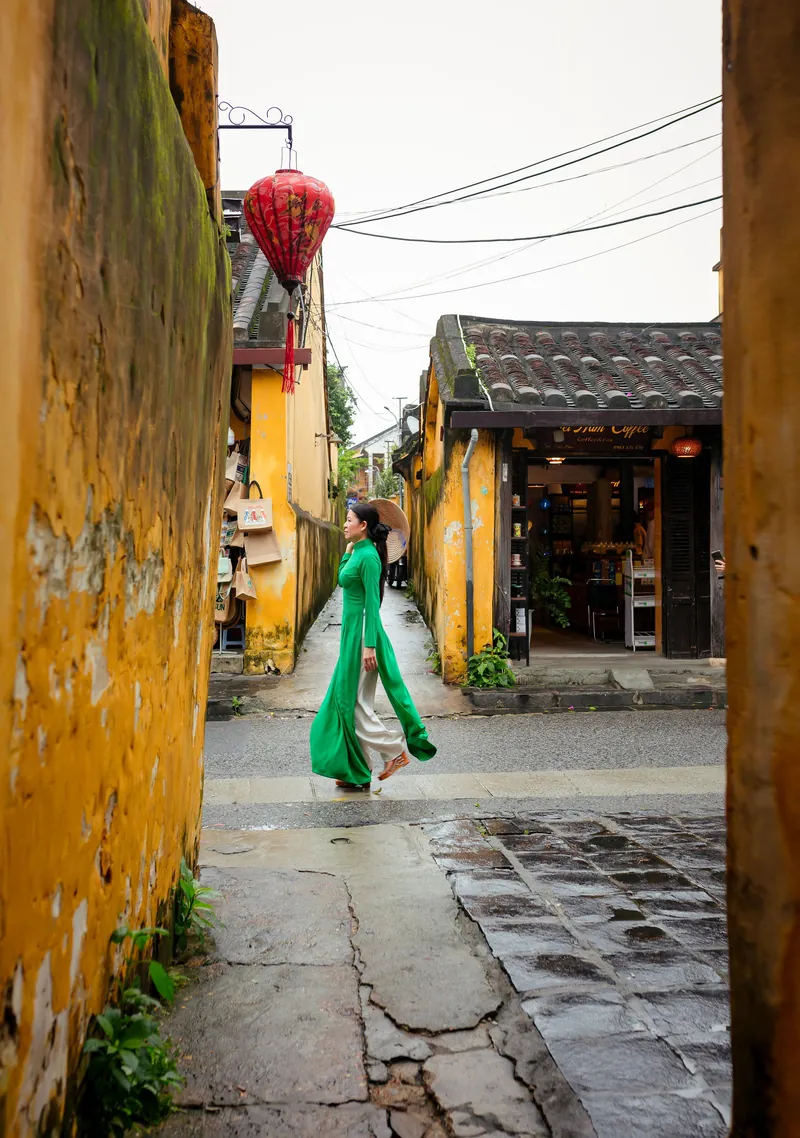 A woman in a green ao dai in a narrow Hoi An street
