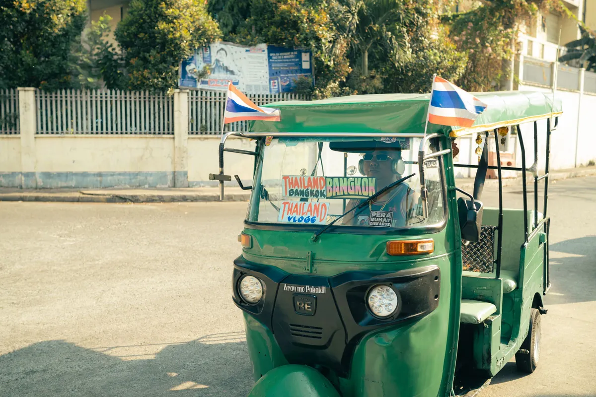 A traditional green tuk-tuk with a driver on a sunny Bangkok street