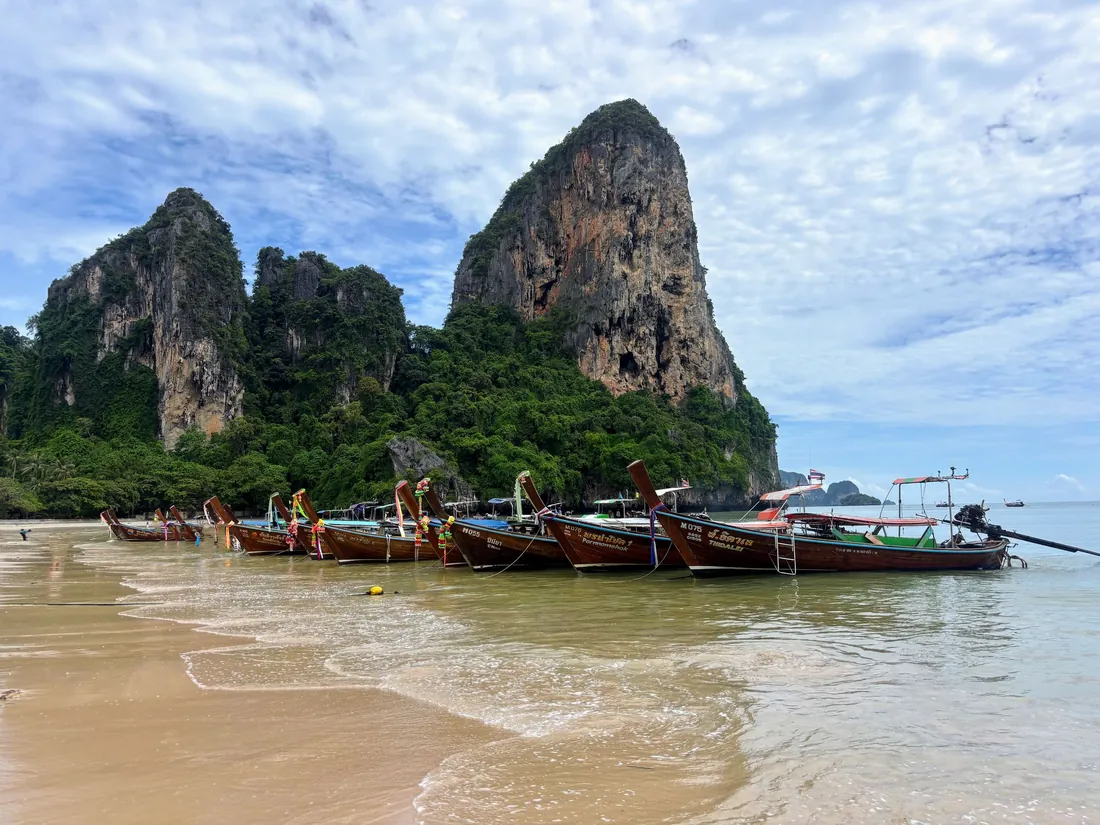 Longtail boats along the shore at Railay Beach in Krabi with limestone cliffs behind
