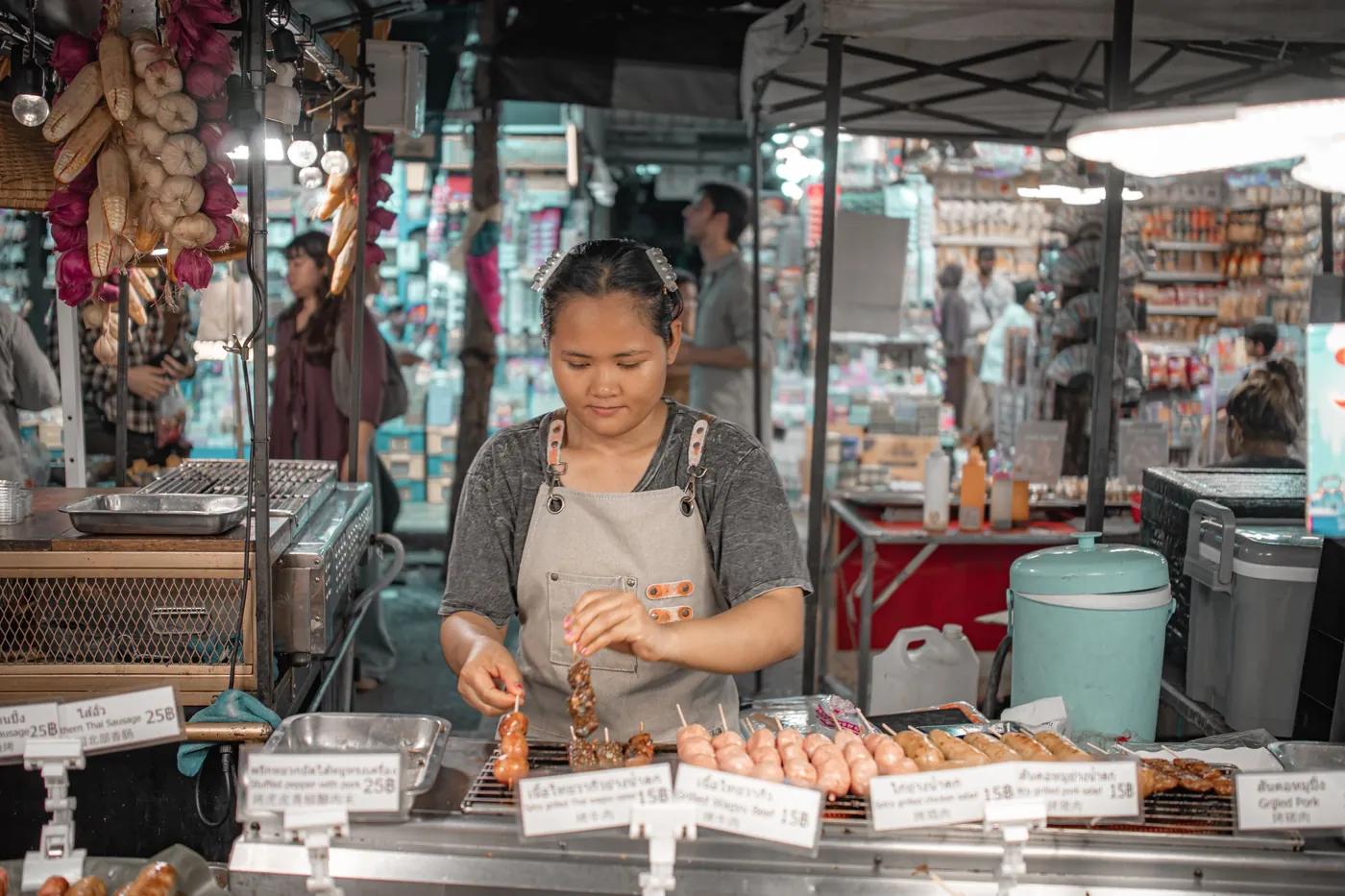 A vendor grilling skewers at a busy Bangkok street market