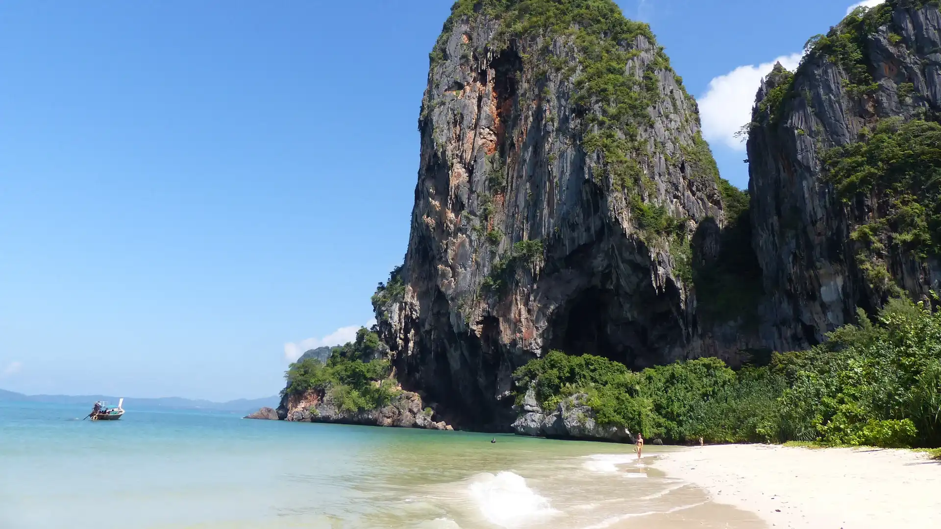 Longtail boat beside a sandy beach and limestone cliffs at Railay in Krabi
